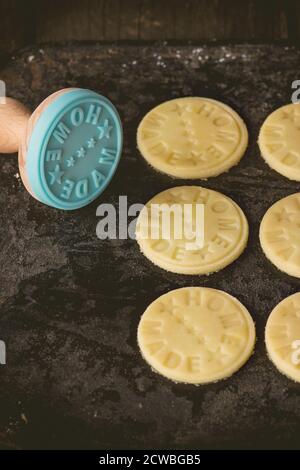 Ungekochte Shortbread, bevor sie gebacken werden, mit blauer Marke mit Aufschrift Home Made. Über schwarzem Schneidbrett. Dunkler rustikaler Stil im Retro-Filter Stockfoto