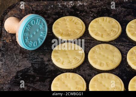 Ungekochte Shortbread, bevor sie gebacken werden, mit blauer Marke mit Aufschrift Home Made. Über schwarzem Schneidbrett. Dunkler rustikaler Stil. Stockfoto