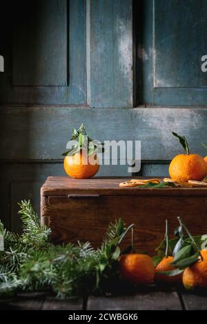 Mandarinen mit Blättern in Weihnachten Einrichtung mit Weihnachtsbaum und trockenen Orange auf hölzernen Kasten über dem alten Holztisch. Dunklen rustikalen Stil Stockfoto