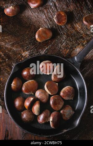 Ungekochte essbare Kastanien in gusseiserner Pfanne über Holztisch. Draufsicht Stockfoto