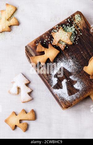 Shortbread Weihnachtsplätzchen für Tassen in Zuckerpulver und kleine Schneidebrett über Tisch mit weißer Tischdecke. Draufsicht. Form wie Weihnachtsbaum, sta Stockfoto