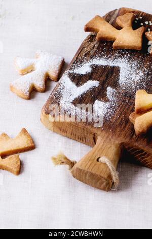 Shortbread Weihnachtsplätzchen für Tassen in Zuckerpulver und kleine Schneidebrett über Tisch mit weißer Tischdecke. Form als Weihnachtsbaum, Sterne und San Stockfoto