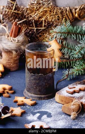 Shortbread Weihnachtsplätzchen für Tassen in Zuckerpulver, Glas heißen Tee in Becherhalter auf Tisch mit blauer Tischdecke. Weihnachtliche Einrichtung im Hintergrund. Sh Stockfoto