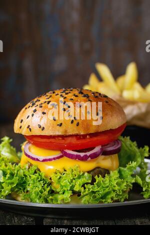 Frisch hausgemachter Burger mit schwarzen Sesamkörnern in altem Metallteller mit pommes Frites Kartoffeln über altem Holztisch mit dunklem Hintergrund. Dunkel rustikal st Stockfoto