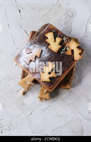 Shortbread Weihnachtsplätzchen für Tassen in Zuckerpulver auf kleinen Holzschneidebrett über grau verputzte Oberfläche. Cookies Formen als Weihnachtsbaum Stockfoto