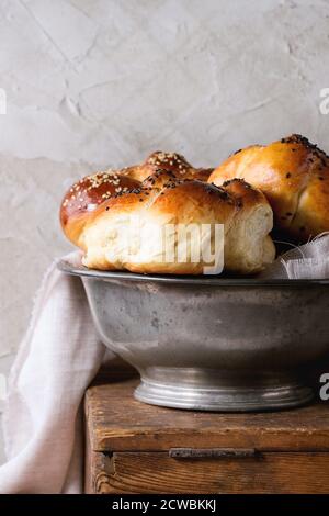 Nahaufnahme des Haufens von süßen runden Sabbath-Challah-Brot Mit weißen und schwarzen Sesamkörnern in Vintage Metallschale Auf Holztisch mit verputzter Wand bei b Stockfoto