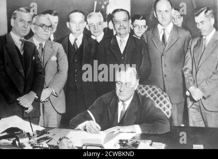 Schwarzweiß-Foto des US-Präsidenten Franklin D. Roosevelt (1882-1945) im Weißen Haus, das ein Dokument unterschrieb, das von seinen wichtigsten Mitarbeitern des Brain Trust umgeben ist, einem Namen, den die engsten Berater des Präsidenten erhielten. Stockfoto