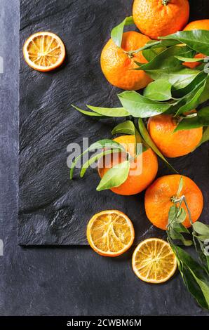 Mandarinen mit Blättern und trocken geschnittenem Orange über schwarzer Schieferfläche. Draufsicht. Stockfoto