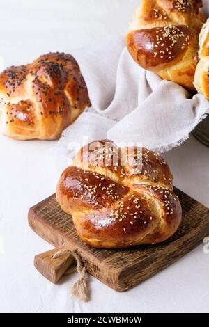 Haufen von süßen runden Sabbath-Challah-Brot mit weißen und schwarzen Sesamsamen auf kleinen Schneidebrett über weißen Tisch mit verputzten Wand im Hintergrund. Stockfoto