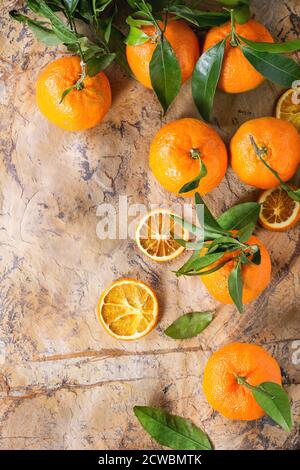 Mandarinen mit Blättern und trocken geschnitten Orange über braun Stein Oberfläche. Ansicht von oben. Stockfoto