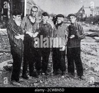 Schwarz-Weiß-Fotografie des Zweiten Weltkriegs (1939-1945) zeigt deutsche Konzentrationslager zum Zeitpunkt ihrer Befreiung durch die Alliierten; eine Gruppe männlicher Häftlinge in gestreiften Hemden blickt auf die Kamera neben einem alliierten Soldaten. Stockfoto