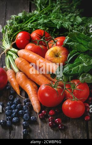 Auswahl von frischem Obst, Gemüse und Beeren Karotten, Spinat, Tomaten, rote Äpfel, Heidelbeeren und Preiselbeeren über alten Holztisch. Stockfoto