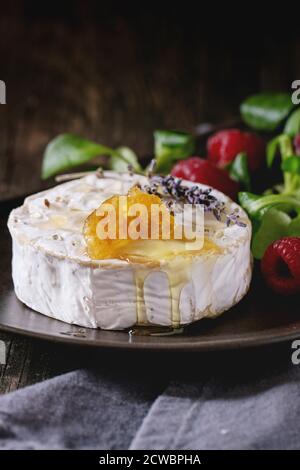 Braun Keramik Teller mit frischem Ziegenkäse, serviert mit Honig, Honig, Lavendel, Himbeeren und grünem Salat auf Grau textile Serviette über alte Holz- Stockfoto