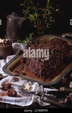 Ganze hausgemachte Weihnachtsschokolade yule log mit Kastanien-Creme auf vintage Tablett mit weißen Textil-Lappen und Kastanien, Schokolade Sterne und Stechpalme Stockfoto