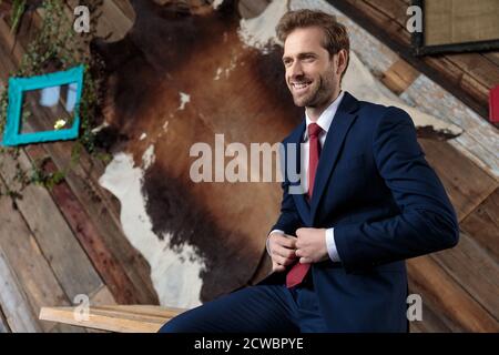 Lächelndes Modelmodell, das zur Seite schaut und Mantel arrangiert, in einem Coffeeshop sitzend Stockfoto