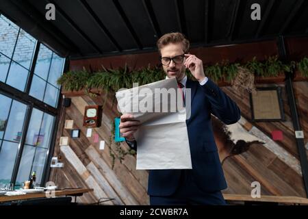 Junger Geschäftsmann im Anzug Nachrichten lesen und justieren Gläser, stehend in einem Coffeeshop Stockfoto