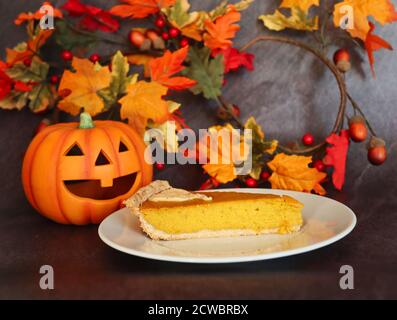 Kürbis Pie Slice mit Keramik Orange Halloween Kürbis und künstliche Herbstblätter. Stück Pie auf weißem Teller mit Herbst und Oktober Dekorationen. Stockfoto