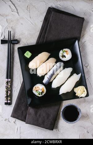 Sushi-Set Nigiri und Brötchen auf schwarzem quadratischen Teller mit Essstäbchen und Sojasauce auf grau verputzter Oberfläche serviert. Flach liegend. Stockfoto