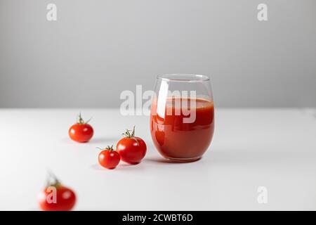 Minimale kreative Komposition mit Glas Tomatensaft und Die Tomaten streuten sich chaotisch auf einem weißen Tisch Stockfoto