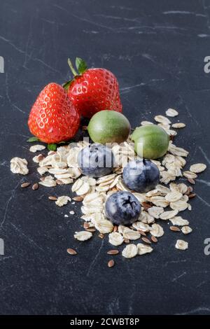 Frische Erdbeeren, Blaubeeren, Kiwi Beeren und Hafer auf schwarzem Marmor Stockfoto