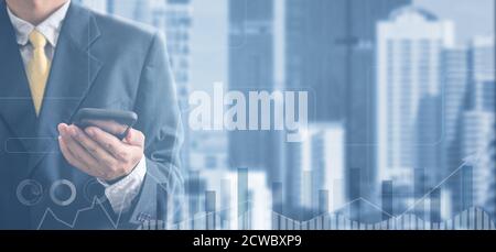 Doppelte Belichtung Hand eines Geschäftsmanns in schwarzem Anzug hält ein Handy auf einem Stadtbild Hintergrund. Analyse von Diagrammen und Diagrammen für das Unternehmenswachstum Stockfoto