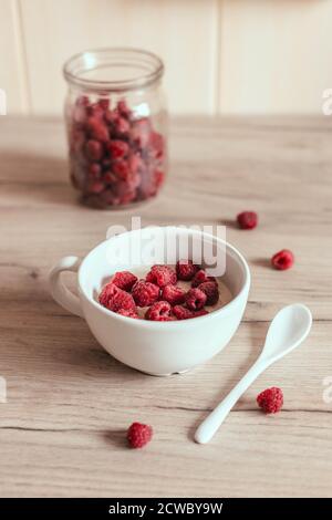 Frischer hausgemachter Haferbrei mit Himbeeren in einer Schüssel auf dem Tisch in der Küche. Leckeres Frühstück. Vertikale Fotoausrichtung Stockfoto