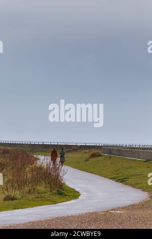 Zwei Frauen genießen einen morgendlichen Spaziergang entlang der Meeresmauer bei Shoeburyness in Essex an einem grauen Septembermorgen Stockfoto