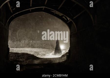 Der Geist einer Frau in einem Kleid, die in einem Tunnel steht, in einer nebligen Nacht. Mit einem Vintage, Sepia, Grunge bearbeiten. Stockfoto