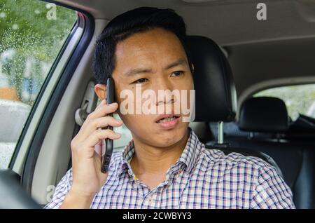 Asian Mann trägt ein kariertes Hemd schaut auf Smartphone in einem Auto. Stockfoto