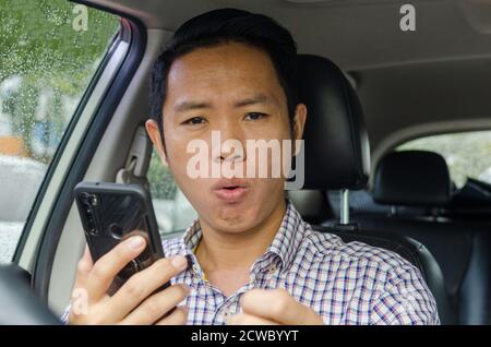 Asian Mann trägt ein kariertes Hemd schaut auf Smartphone in einem Auto. Stockfoto