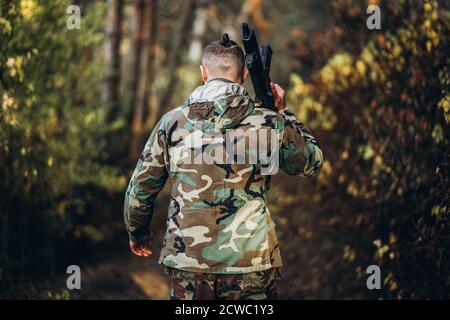 Ein Soldat in Tarnuniform mit einem Gewehr auf der Schulter geht im Wald. Rückansicht. Airsoft. Stockfoto