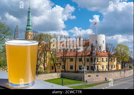 Ein Glas leichtes Bier mit Blick auf die Burg von Riga während eines sonnigen Tages in Riga, Lettland. Die Rigaer Burg ist eine Burg am Ufer des Flusses Daugava. Stockfoto