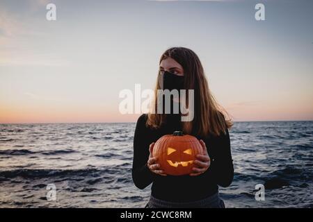 Frau trägt Schutzmaske halten Jack o Laterne Kürbis Stockfoto