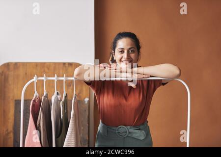 Porträt einer jungen Verkäuferin, die in der Nähe des Racks mit neuen steht Kleidung und lächelnd an der Kamera arbeitet sie im Geschäft Stockfoto