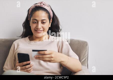 Junge lächelnde Frau, die online mit ihrem Handy und einkaufen Zahlung mit Kreditkarte Stockfoto