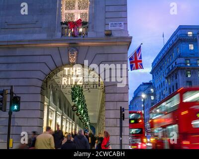 The Ritz Hotel zu Weihnachten festliche Jahreszeit, abends Lichter ‘The Ritz’ Schild beleuchtet, mit einer Union Jack Flagge, Einkäufer und vorbei an London roten Bussen Arlington Street Piccadilly London UK Stockfoto