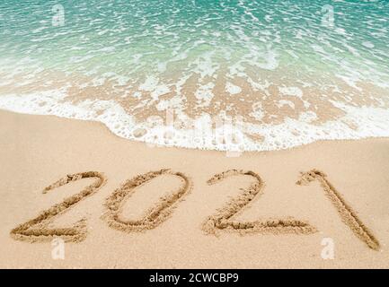 Frohes neues Jahr 2021, Schriftzug am Strand mit Welle und blauem Meer. Zahlen 2021 Jahr an der Küste, Neujahrs-Konzept. Stockfoto