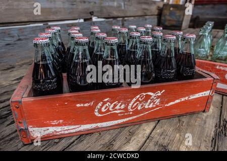 Vintage Coca-Cola mit Cola noch in den Glasflaschen Eine hölzerne Lieferkiste, die auf einem alten Holzboden sitzt Nahaufnahme im Innenbereich Stockfoto