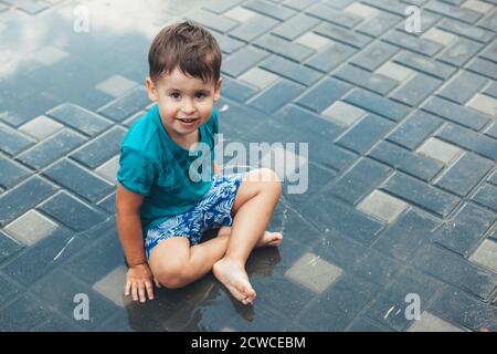 Lächelnder kaukasischer Junge, der die Kamera anschaut und lächelt Spielen Sie im Wasser auf dem Boden Stockfoto