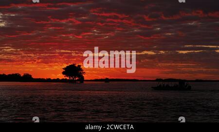 Atemberaubende Aussicht über Chobe River im Abendlicht nach Sonnenuntergang mit schönen roten Wolken und den Silhouetten von zwei Safaribooten. Stockfoto