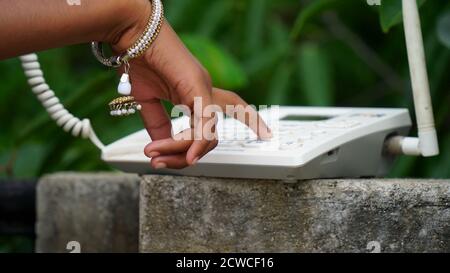 Nahaufnahme des weiblichen Hand-Telefonempfängers beim Wählen einer Telefonnummer, um einen Anruf mit einem weißen Festnetztelefon zu tätigen. Stockfoto