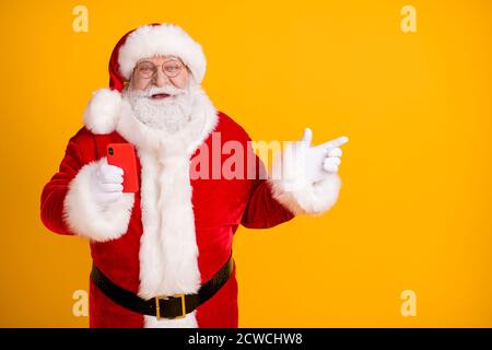 Aufgeregt weihnachtsmann mit großen Bauch verwenden Handy-Suche Weihnachten Magische Fee weihnachtsabend Rabatt Anzeigen Point Finger Copyspace tragen Kopfbedeckung Gürtel Stockfoto