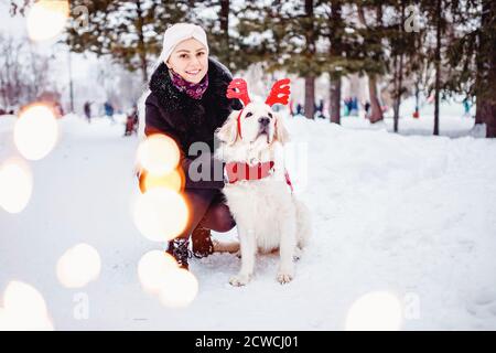 Weihnachtskostüm für Hund, junge schöne Mädchen geht mit goldenen Retriever im Winterwald Stockfoto