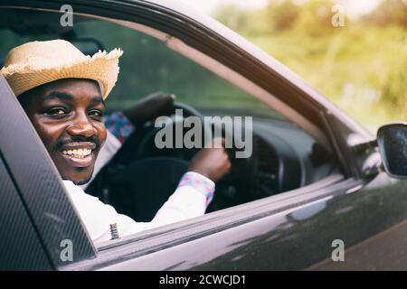 Afrikanischer Mann Fahrer trägt einen Hut und lächelt während des Sitzens In einem Auto mit geöffneter Frontscheibe Stockfoto