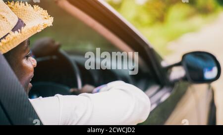 Afrikanischer Mann Fahrer trägt einen Hut und lächelt während des Sitzens In einem Auto mit geöffneter Frontscheibe Stockfoto