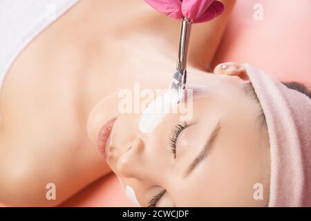 Arzt wendet Anti Falten Aging Creme Haut der jungen Frau im Schönheitssalon, rosa Hintergrund Stockfoto
