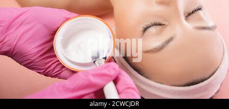 Arzt wendet Anti Falten Aging Creme Haut der jungen Frau im Schönheitssalon, rosa Hintergrund Stockfoto