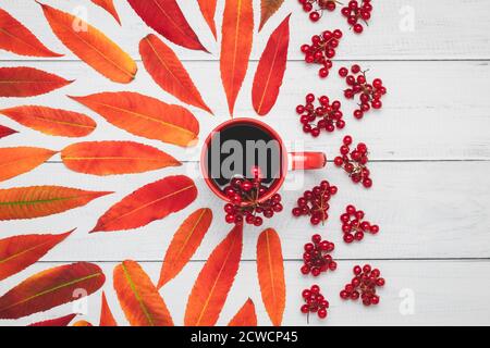 Eine Tasse Tee mit Viburnum-Beeren und roten Herbstblättern auf Holzbrettern, Oktoberstimmung, rustikale Komposition, bunte kreative Abstraktion mit Kunst Stockfoto