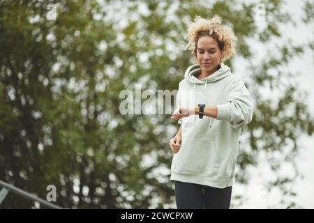 Junge Frau, die ihren Puls während ihrer Zeit auf der Uhr überprüft Joggen im Park Stockfoto