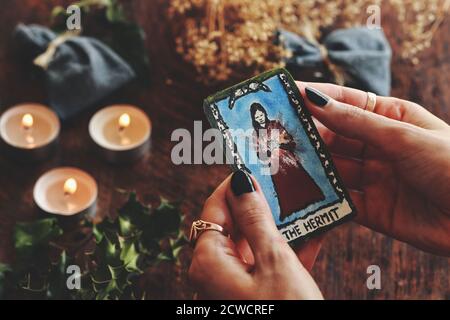 Wiccan Hexe hält eine kleine Hand bemalte (ermachte) Einsiedler Tarot-Karte in ihren Händen. Gemütliche warme Yule Winter Sonnenwende (Weihnachten) Hintergrund Stockfoto